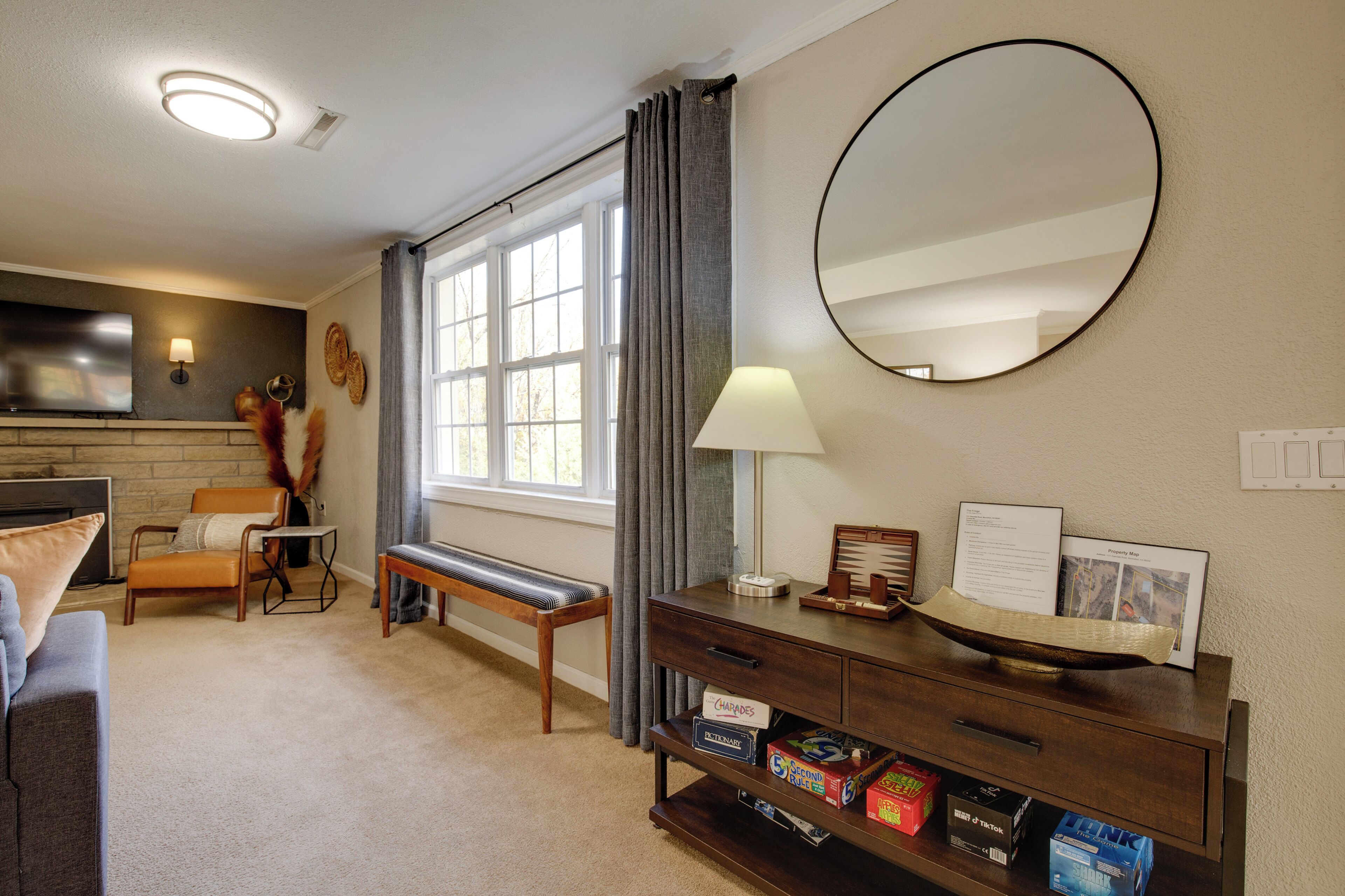 A living room with a fireplace, a sofa, a bench, a coffee table, a lamp, a mirror, and a bookshelf with books and decorative items.