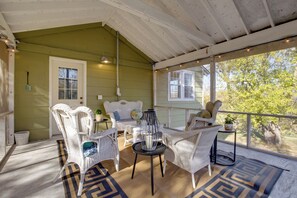 Eine überdachte Veranda mit Korbmöbeln, einem Tisch und Blick auf Bäume.