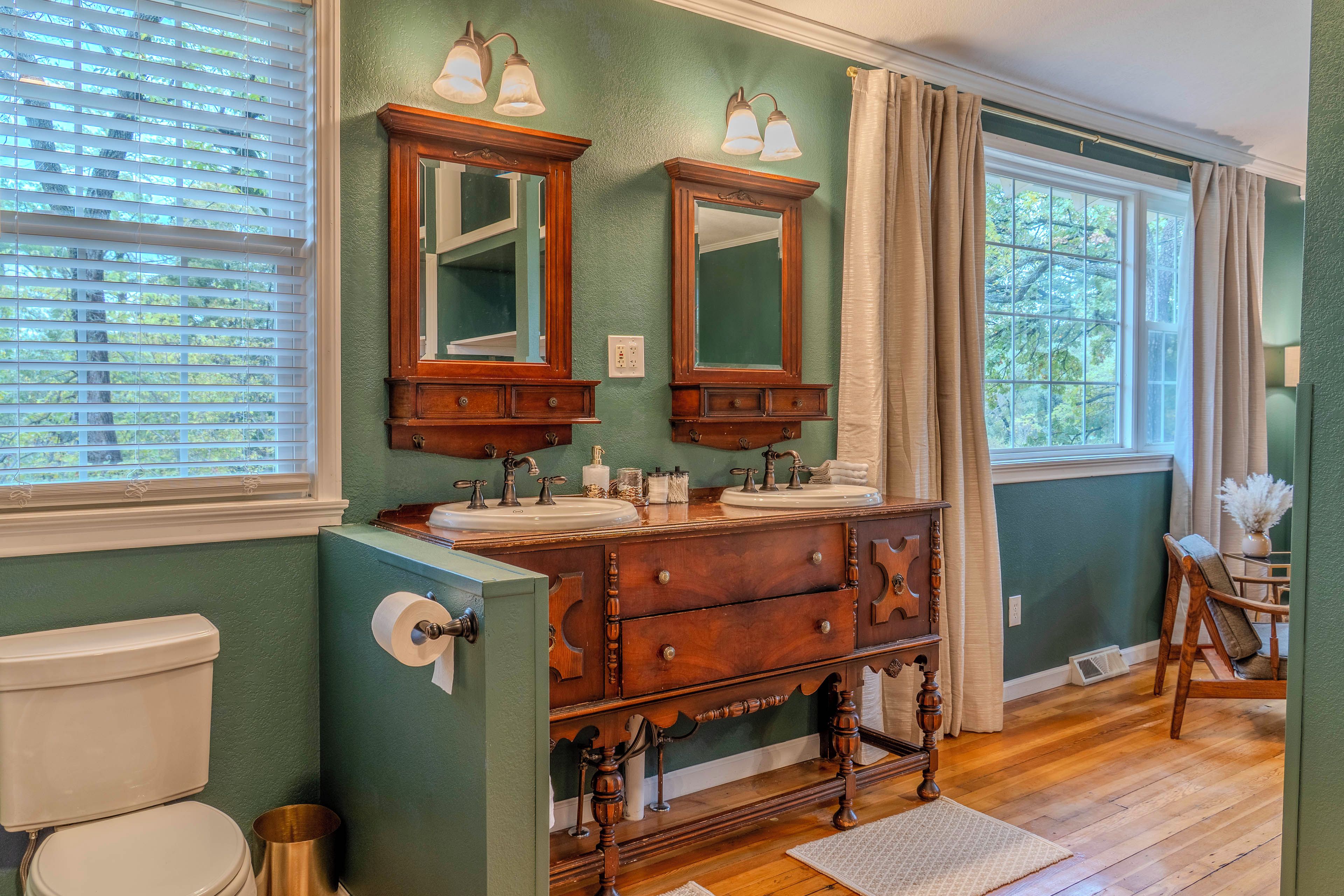 A bathroom with two sinks, wooden vanity, and a window with curtains.
