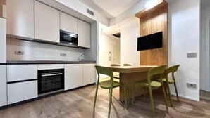 A modern kitchen with white cabinets, a built-in oven, and a dining area with a wooden table and green chairs.