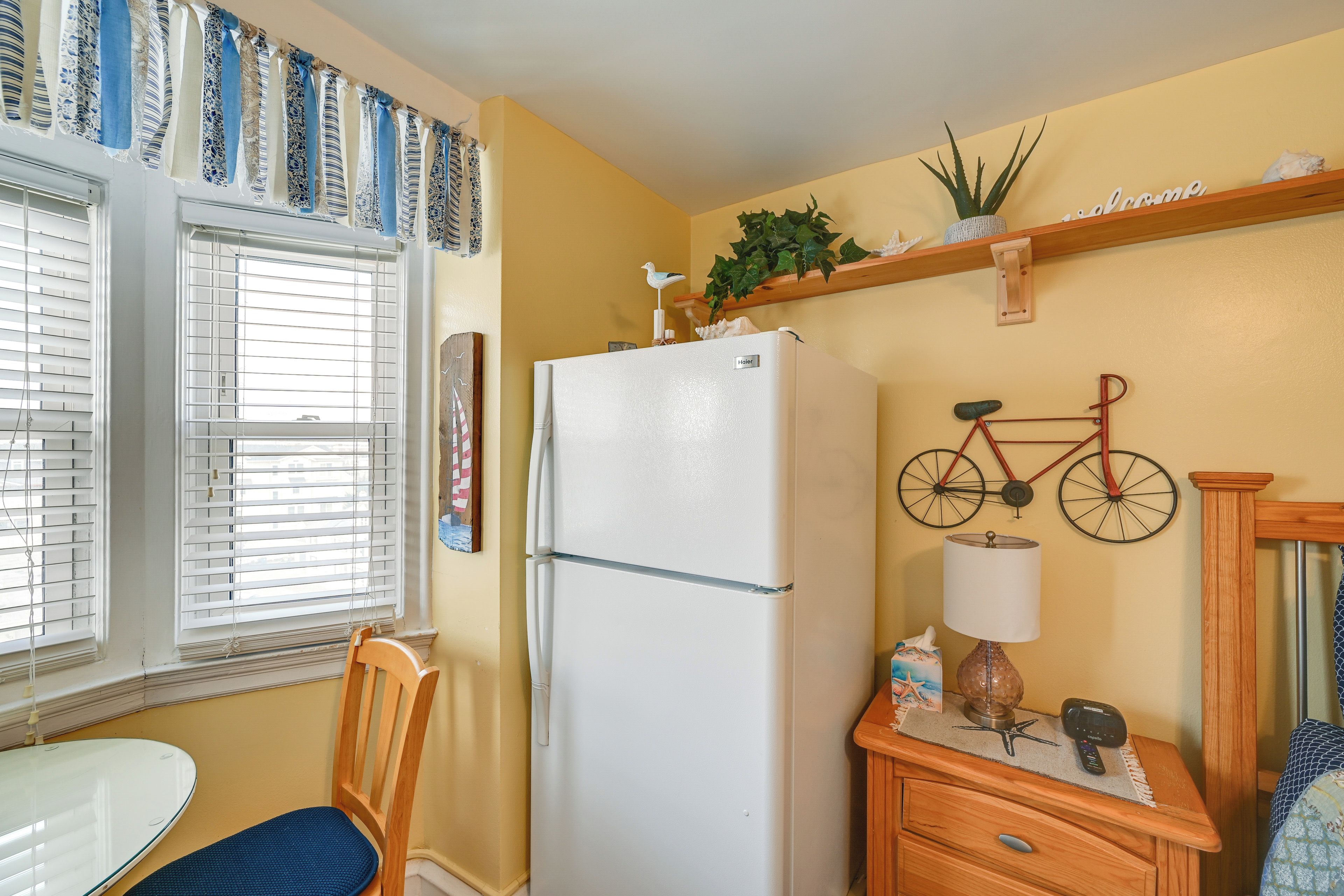 A compact kitchen with a refrigerator, a dining table with a chair, a wooden cabinet, and a bicycle mounted on the wall.
