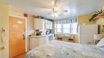 Habitación compacta con cama, kitchenette, zona de comedor y ventilador de techo.
