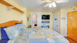 Ein Schlafzimmer mit einem Bett, einem Deckenventilator, einer Tür und einem kleinen Tisch mit einem Bilderrahmen.