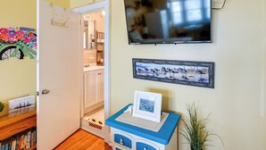 A room with a television mounted on the wall, a door leading to another room, and a small table with a picture frame. - Bay & Bridge Views! Walkable Ocean City Condo (Ocean City)