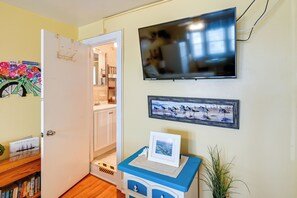 A room with a television mounted on the wall, a door leading to another room, and a small table with a picture frame. - Bay & Bridge Views! Walkable Ocean City Condo (Ocean City)