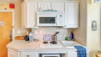 A compact kitchen with white cabinets, a microwave, a stove, and a sink.