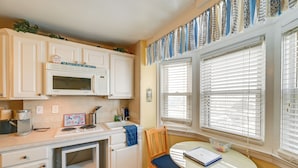 A kitchen with white cabinets, a microwave, a coffee maker, and a small table with a chair. - Bay & Bridge Views! Walkable Ocean City Condo (Ocean City)