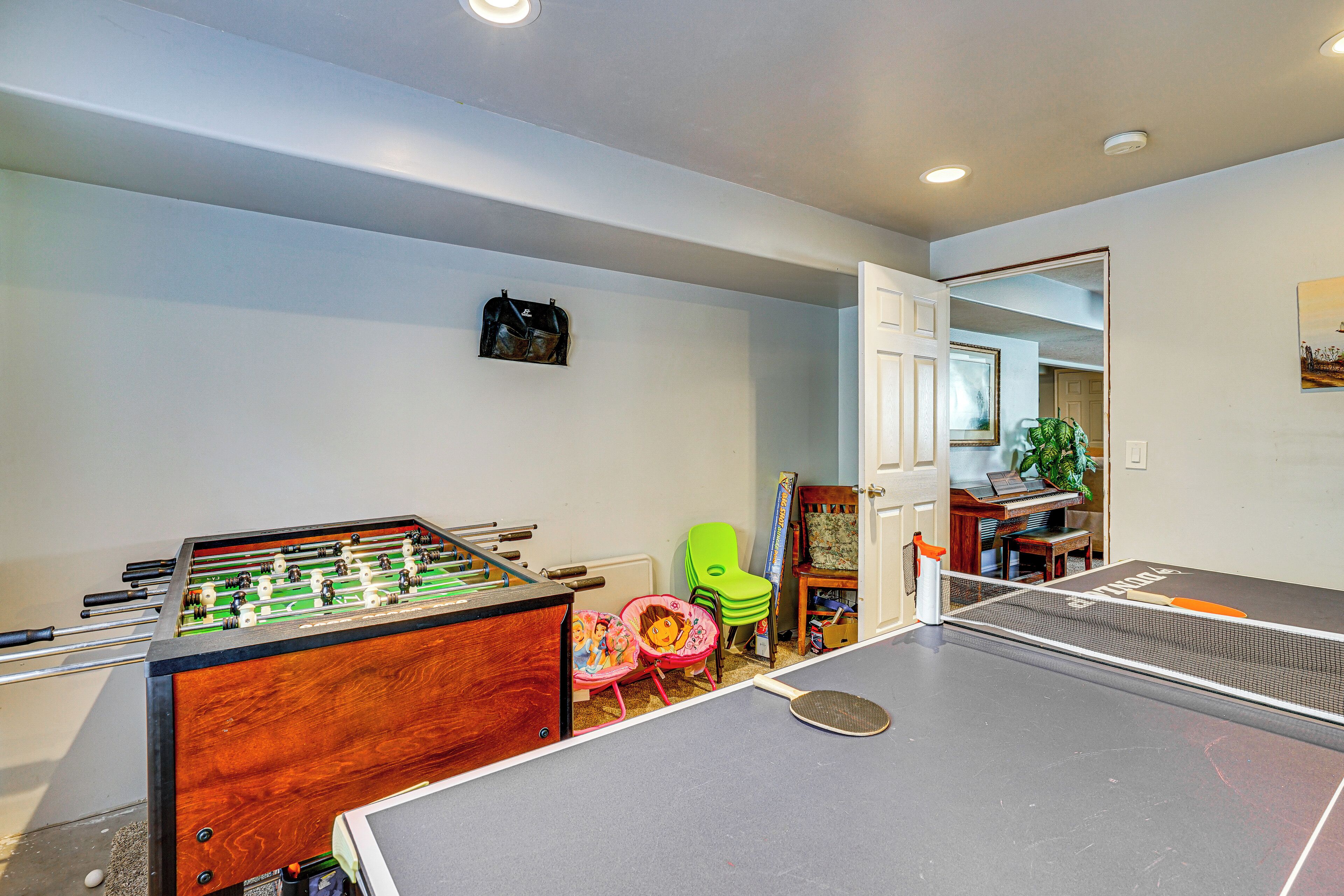 A room with a foosball table, ping pong table, and chairs.