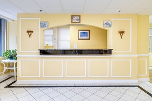 Une salle d’attente avec un mur jaune, des moulures blanches et un sol carrelé. On y trouve deux appliques murales et un tableau encadré au-dessus du comptoir d’accueil.