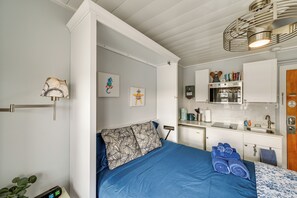 Une chambre compacte comprenant un lit, des oreillers et une table de chevet avec une lampe. À côté se trouve une petite cuisine équipée d’un four à micro-ondes, d’un évier et de placards.