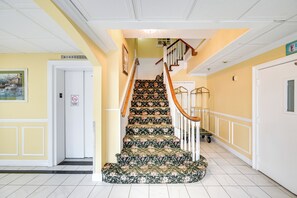 Un escalier recouvert d’une moquette à motifs floraux, des murs blancs et une porte jaune.