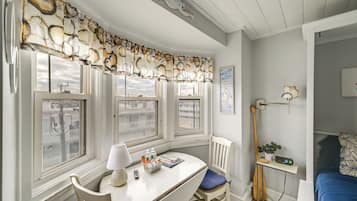 A room with a white desk, a chair, a lamp, and a window with a view of buildings.