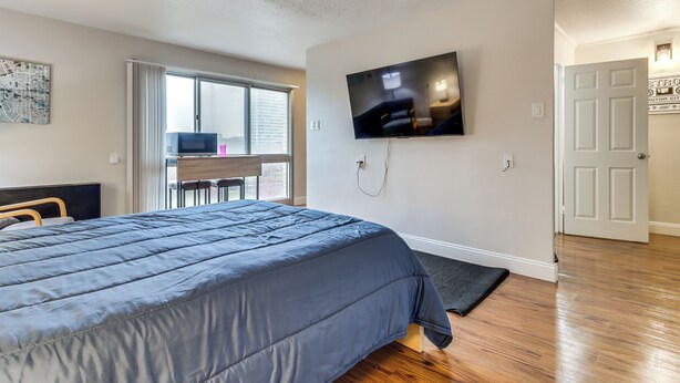 A bedroom with a bed, a TV mounted on the wall, a desk with a chair, and a door. - 2 Mi to DMC & Children's Hospital: Modern Studio (Detroit)