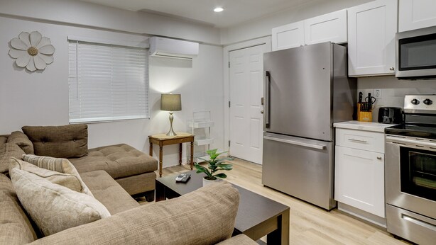 A modern kitchen with white cabinets, a stainless steel refrigerator, and an oven. There is a dining area with a brown sofa and a small table. - 10 Mi to Riverside! Apt Near Ruhs Medical Center (Moreno Valley)
