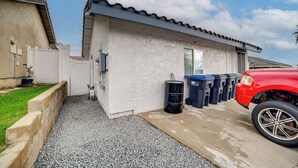 A residential building with a concrete exterior, a red car parked in front, and several black trash bins lined up outside. - 10 Mi to Riverside! Apt Near Ruhs Medical Center (Moreno Valley)