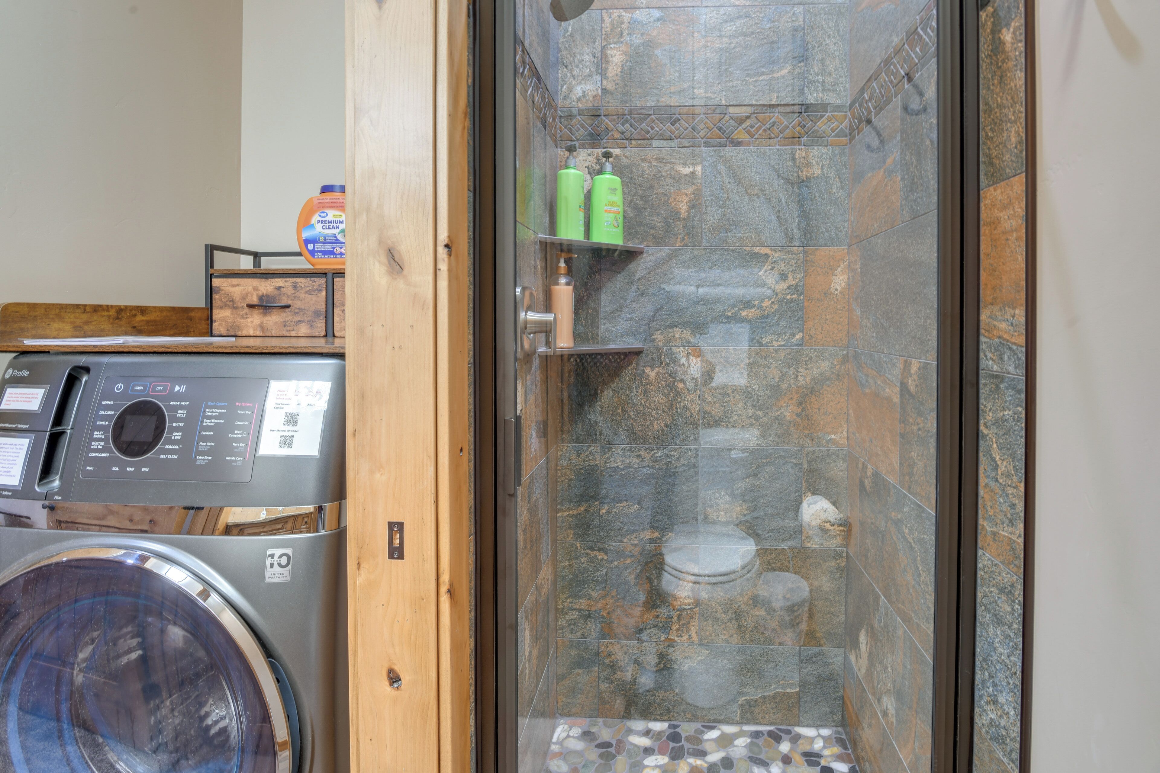 A laundry area with a washing machine, a dryer, and a glass-enclosed shower stall with a tiled shower floor.