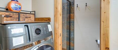 Un espace buanderie compact comprenant un lave-linge et un sèche-linge à chargement frontal, un meuble de rangement en bois et une cabine de douche en verre.