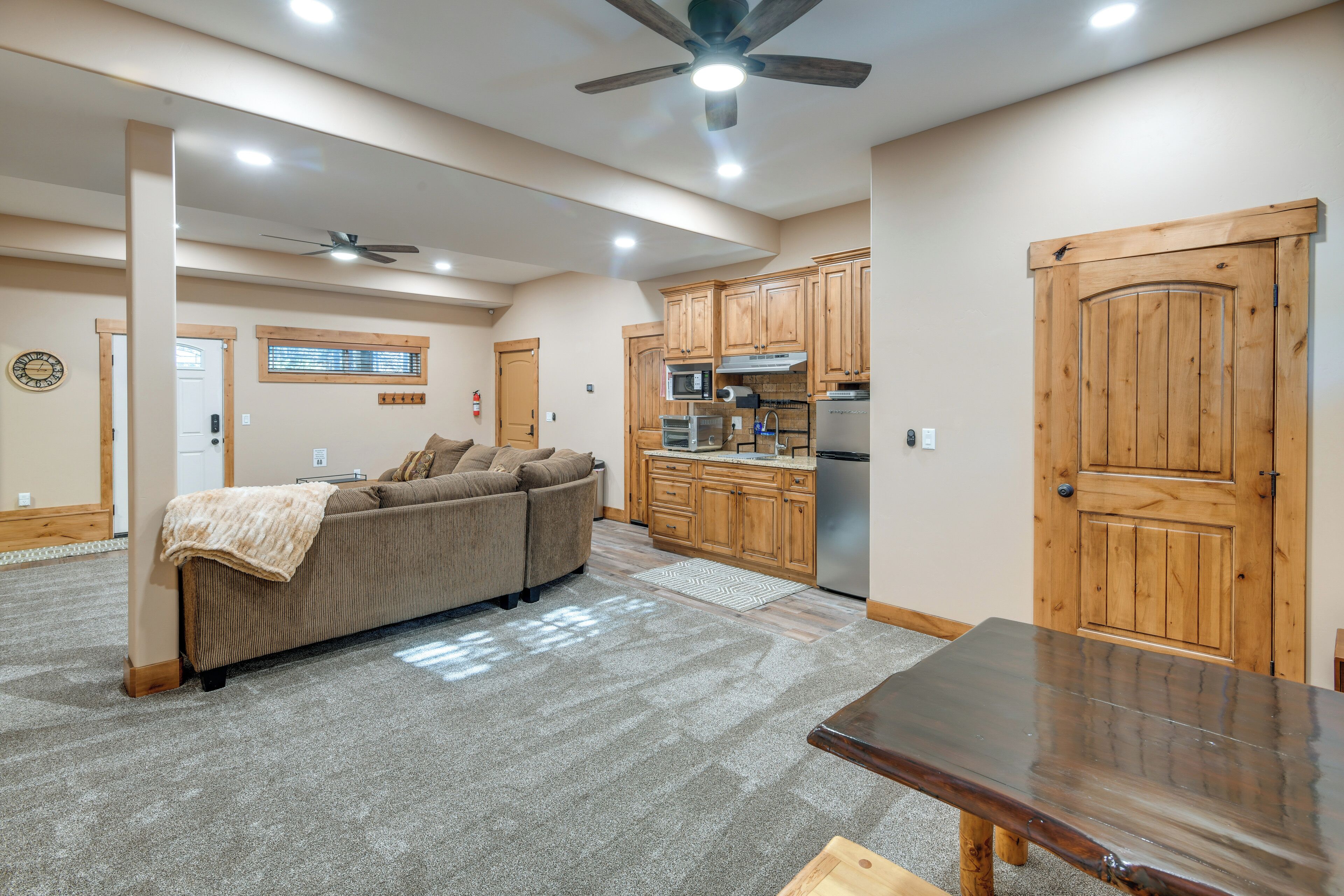 A spacious living area with a sofa, a wooden dining table, and a kitchen with wooden cabinets and appliances.