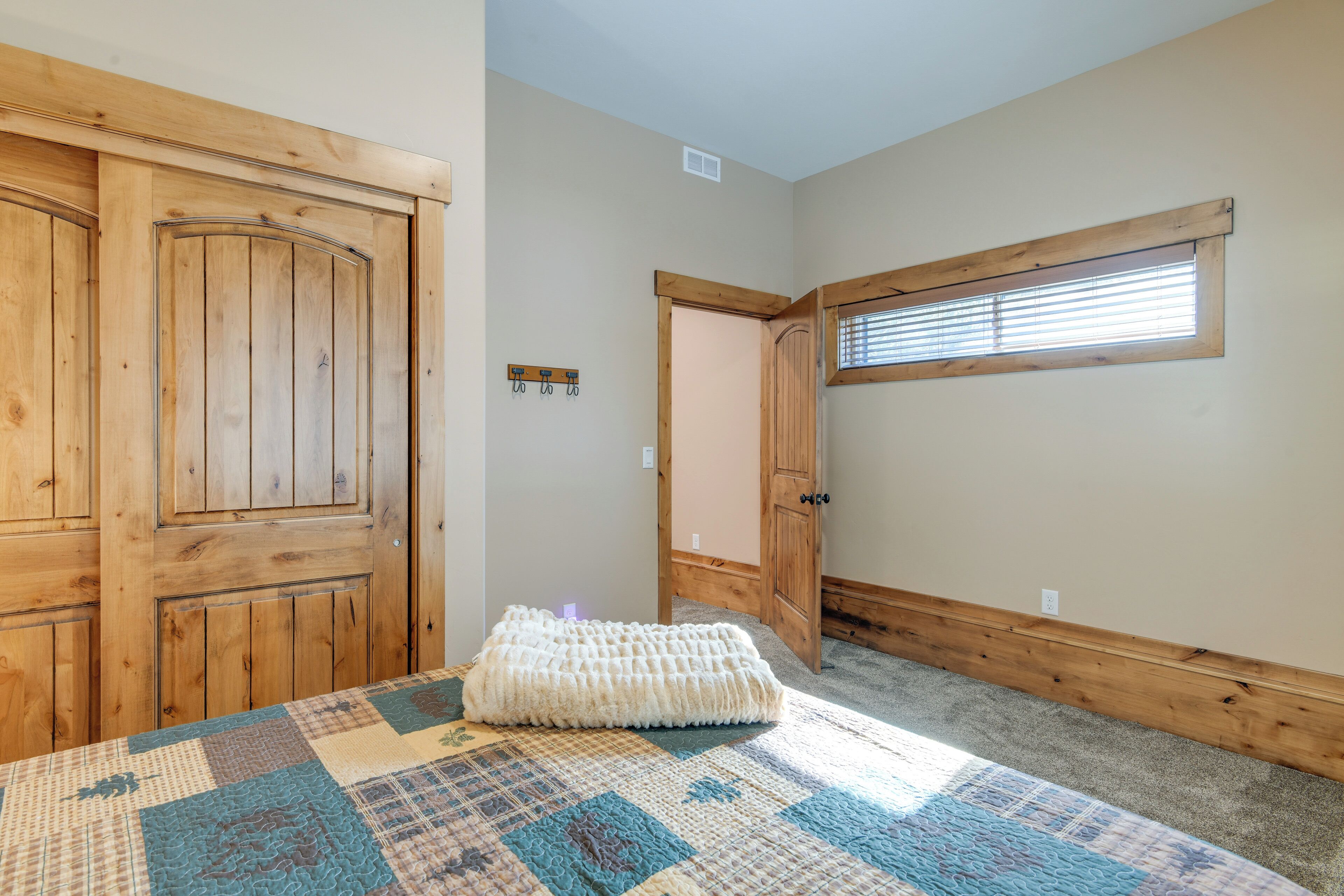 A room with wooden doors, a quilted bedspread, a window with blinds, and a small wall-mounted light fixture.