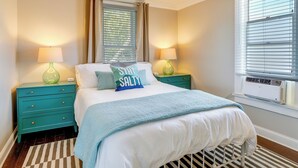 Une chambre à coucher comprenant un lit, deux tables de chevet, une fenêtre avec des stores et un ventilateur de plafond.