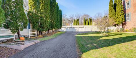 A driveway leading to a house with a garage, surrounded by tall trees and a well-maintained lawn.