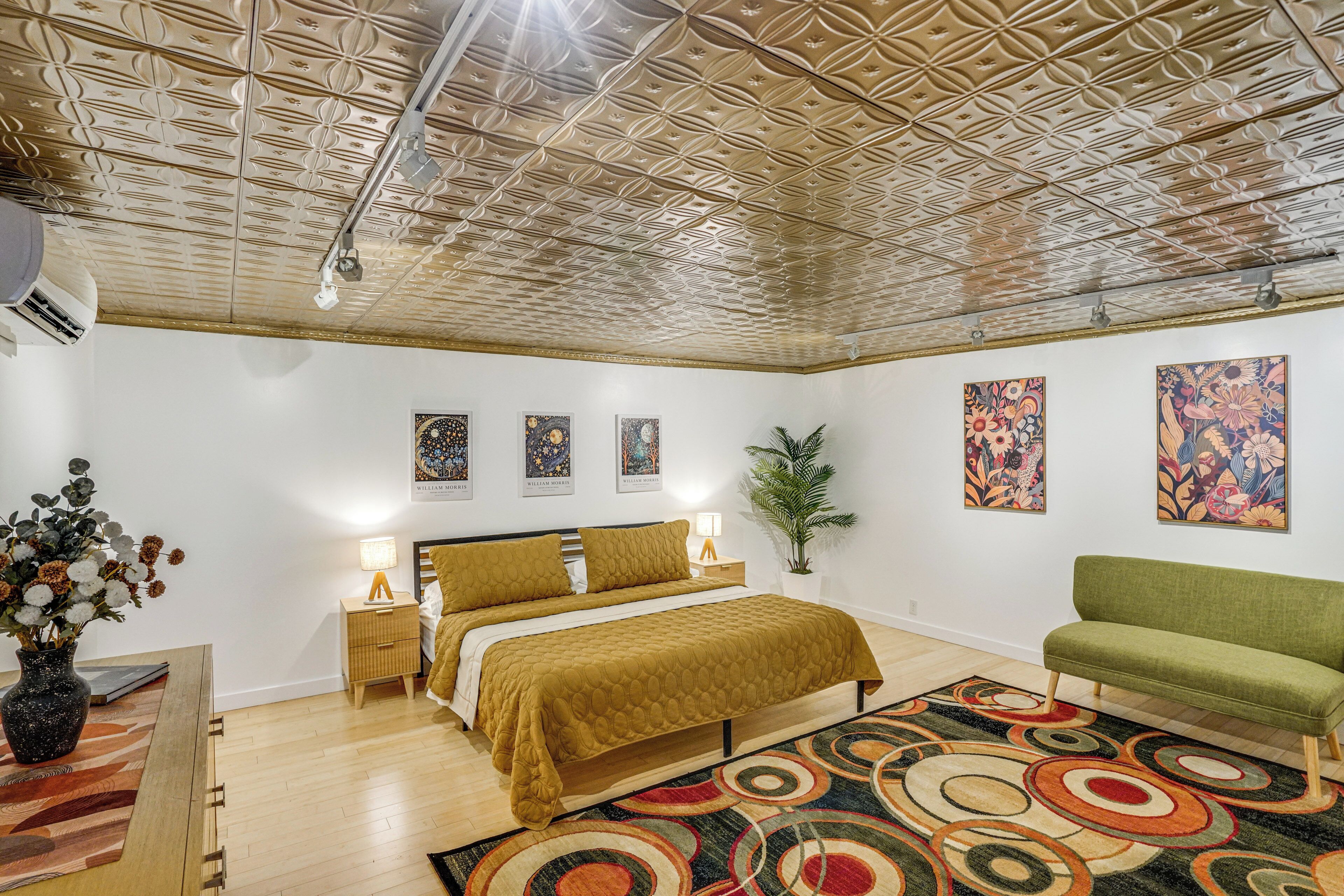 A bedroom with a bed, bedside tables, a green sofa, a patterned rug, and artwork on the walls.