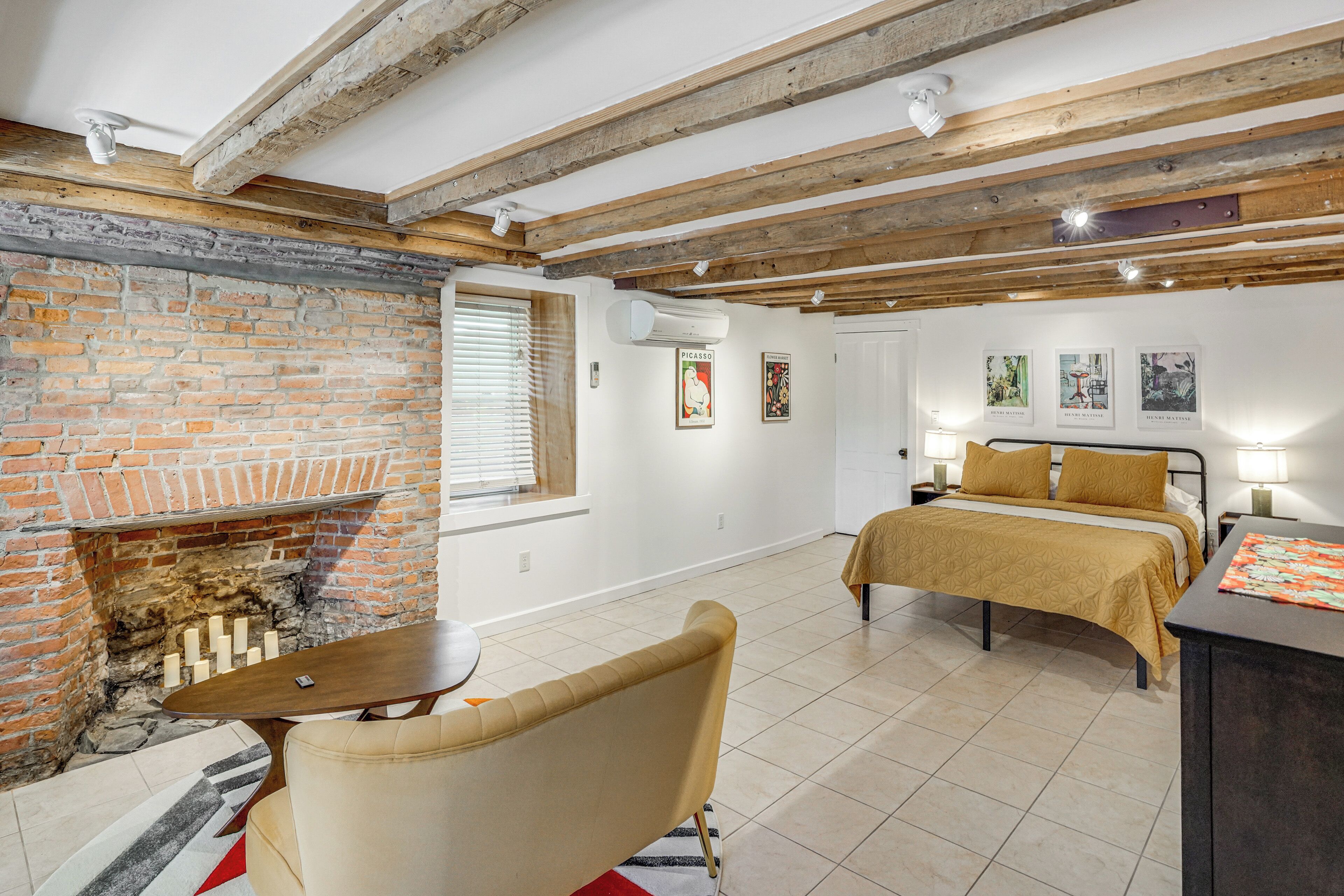 A room with a brick fireplace, a bed with a yellow bedspread, a wooden table, and a chair.