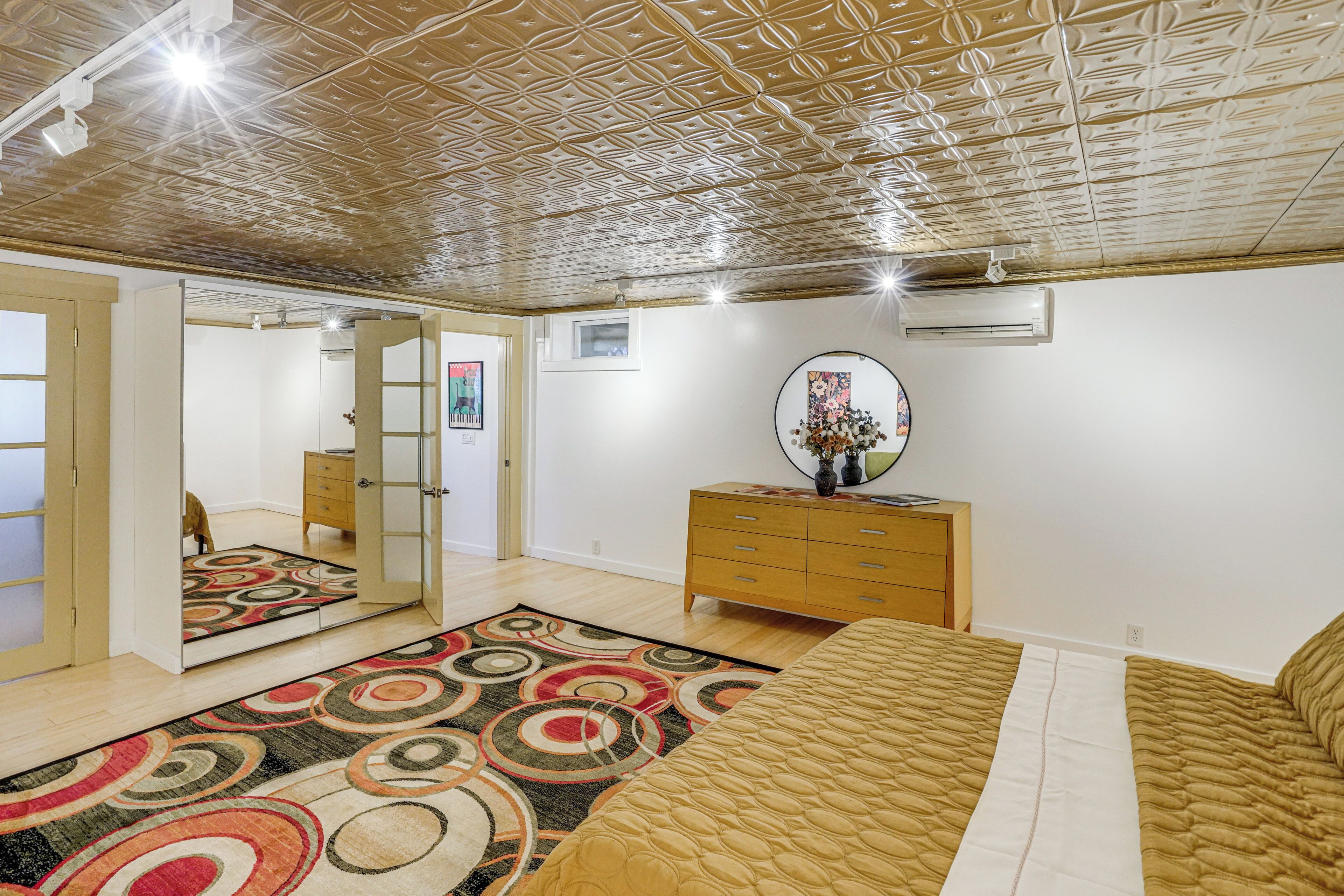 A bedroom with a patterned carpet, a bed, a dresser, a mirror, and a ceiling with a geometric design.