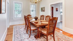 Une salle à manger avec une table en bois, des chaises, un lustre et un tapis à motifs.