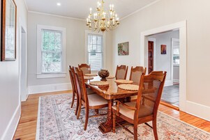 Comedor con mesa de madera, sillas, una lámpara de araña y un tapete estampado.