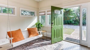 Une pièce avec un banc blanc, une porte verte et une vue sur l’extérieur.