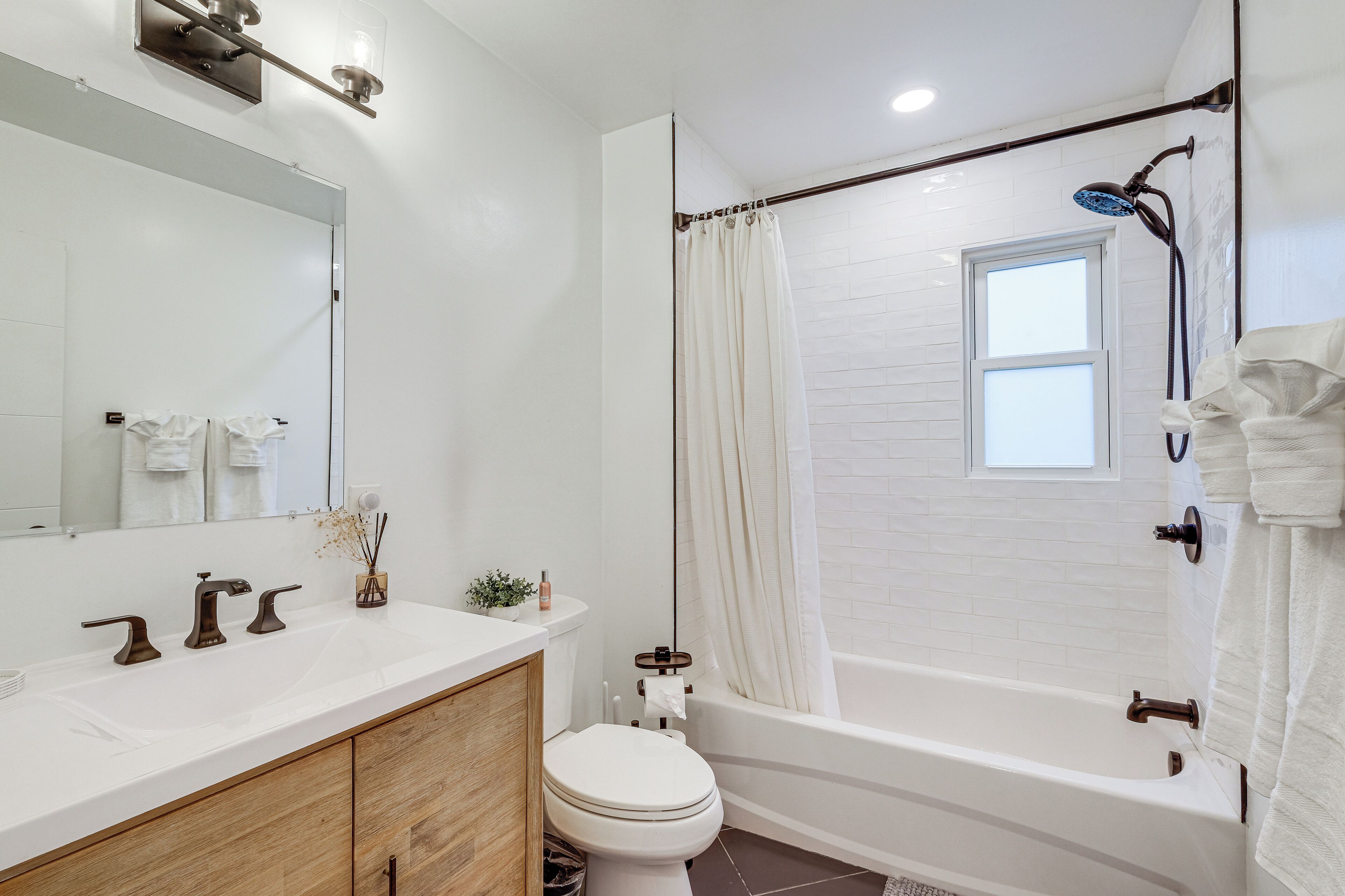 A modern bathroom with a white sink, wooden cabinet, toilet, and a bathtub with a showerhead.