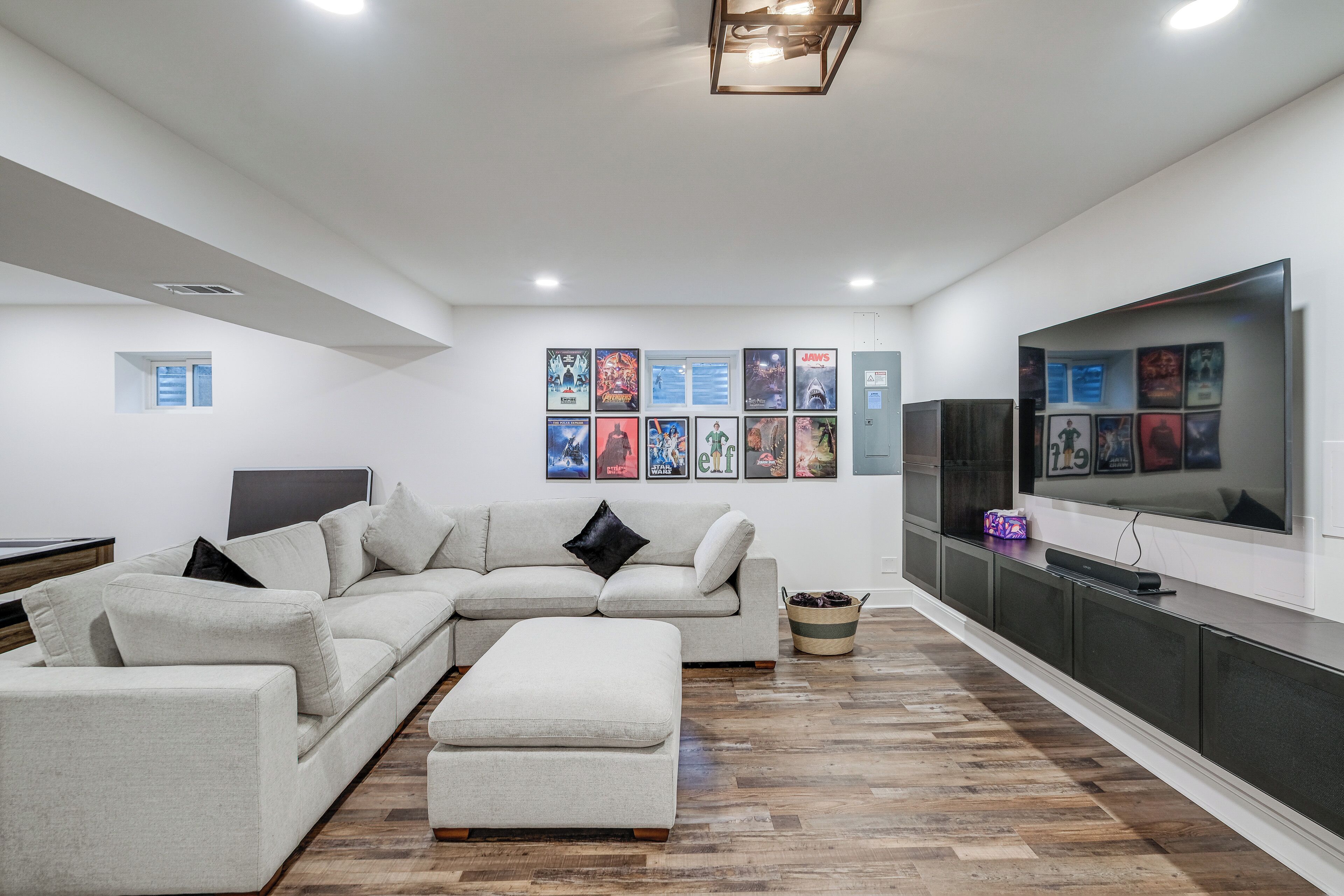 A modern living room with a sectional sofa, a flat-screen TV, and a wall decorated with movie posters.