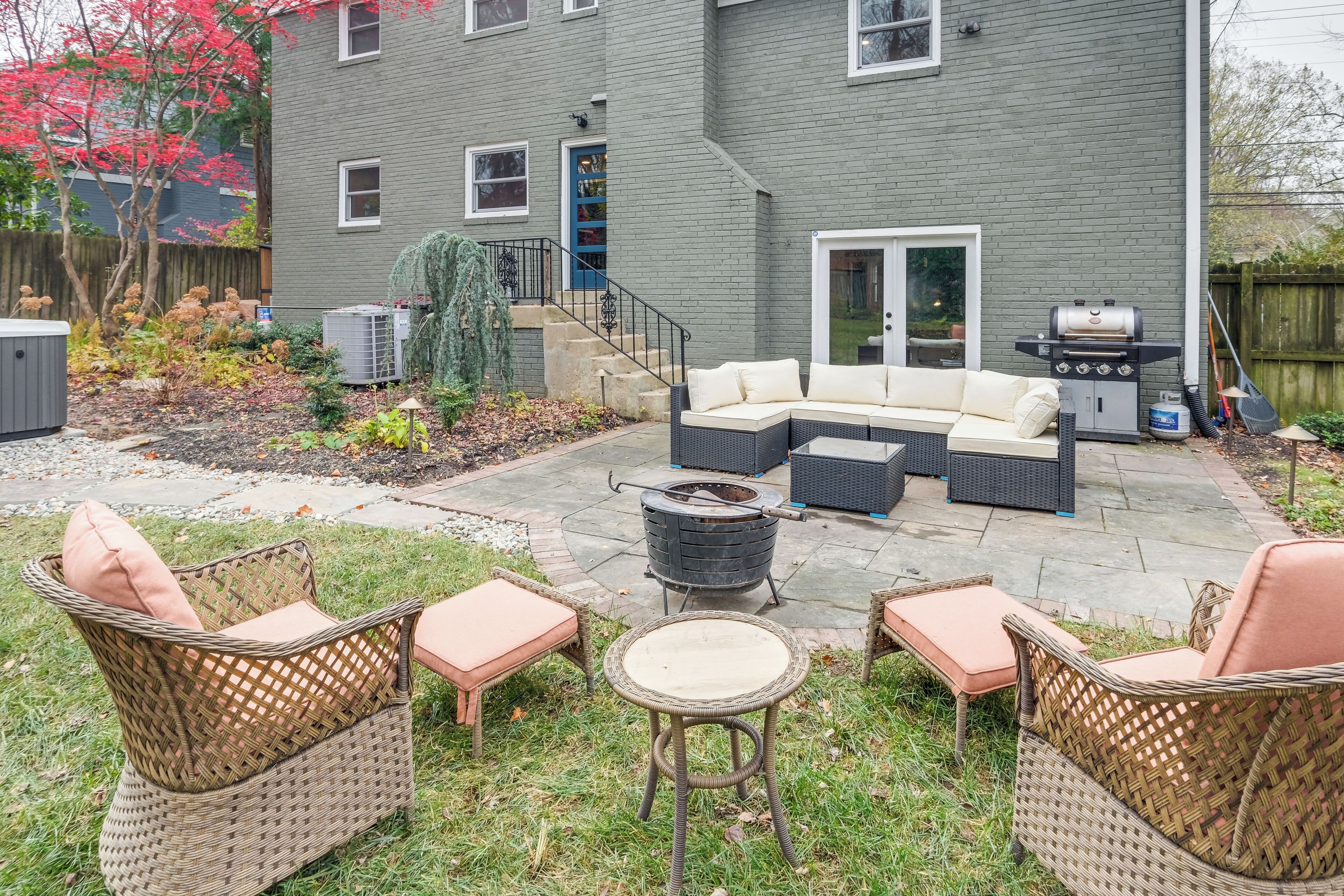 A backyard with a gray house, outdoor furniture, a grill, and a fire pit.