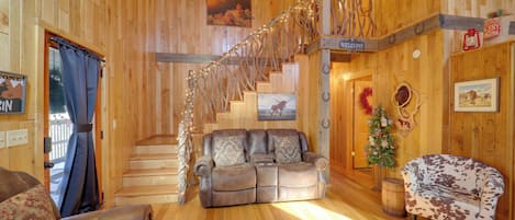 A wooden interior with a sofa, a patterned armchair, a staircase, and a Christmas wreath.