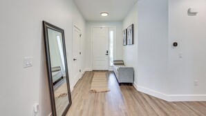 A hallway with hardwood floors, white walls, a mirror, a door, and a gray bench. - Stone's Throw to All Major Attractions: Family Gem (North Port)
