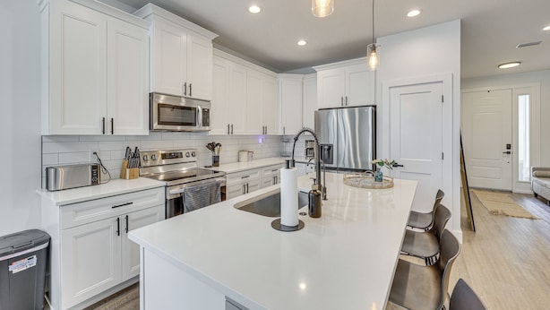 A modern kitchen with white cabinetry, stainless steel appliances, a central island with seating, and pendant lighting. - Stone's Throw to All Major Attractions: Family Gem (North Port)
