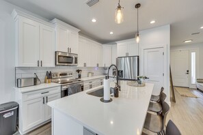 Una cocina moderna con armarios blancos, electrodomésticos de acero inoxidable, una isla central con asientos e iluminación colgante.