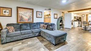 A living room with a grey sectional sofa, wooden flooring, and framed artwork on the walls.