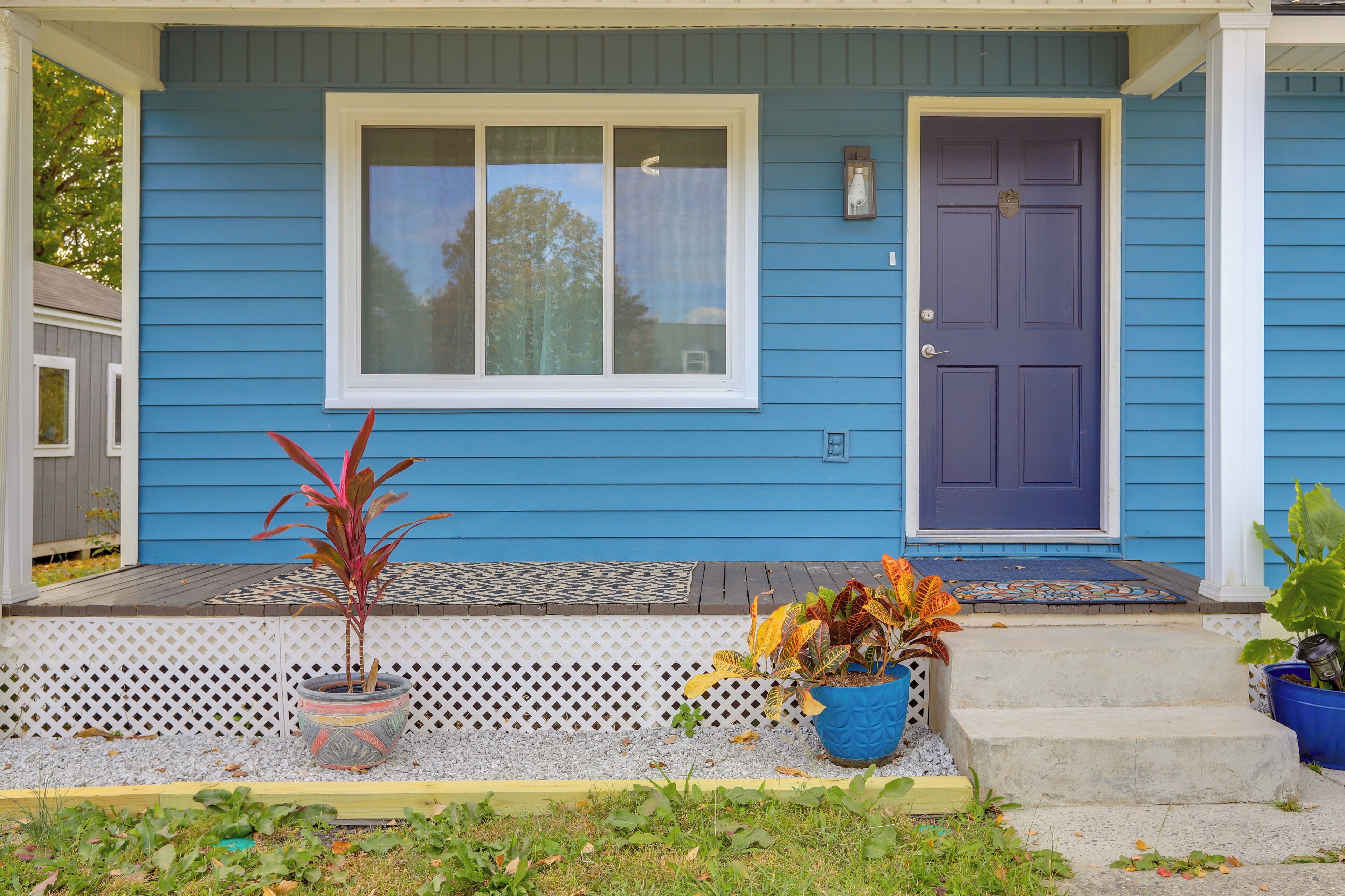 A blue house with a front porch, a purple door, and potted plants.