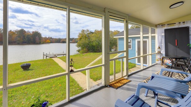 A covered patio with a view of a lake, outdoor furniture, and a blue building in the background. - Lakefront Getaway w/ Dock & Views in Macon! (Macon)