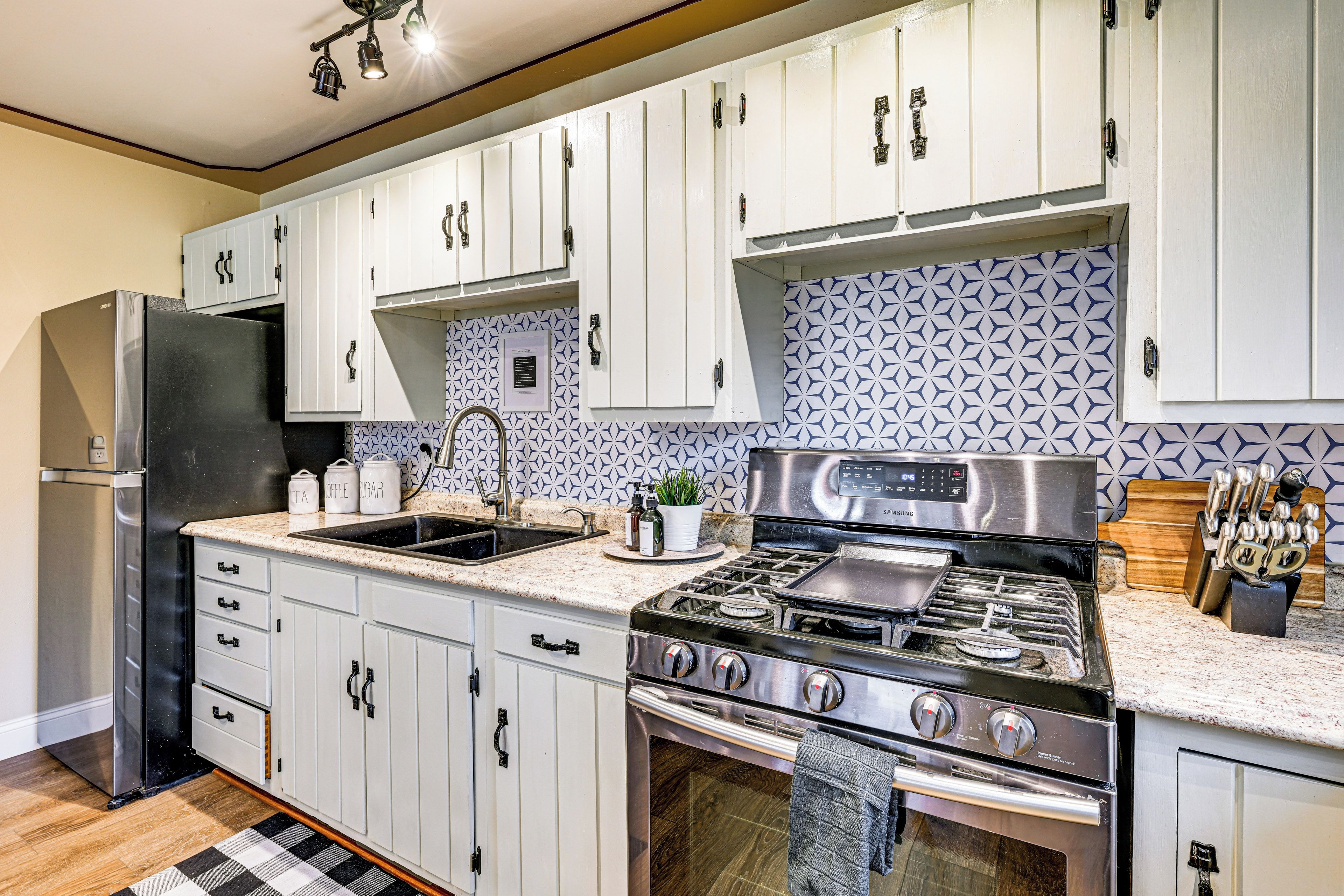 A modern kitchen with white cabinets, a stainless steel refrigerator, a gas stove, and a sink.