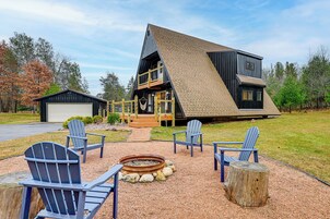 Una casa moderna de dos pisos con un amplio balcón, zona de estar exterior con sillas Adirondack y una chimenea.