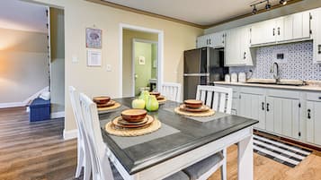 Cocina moderna con armarios blancos, un refrigerador negro y una zona de comedor con una mesa de madera oscura y sillas blancas.