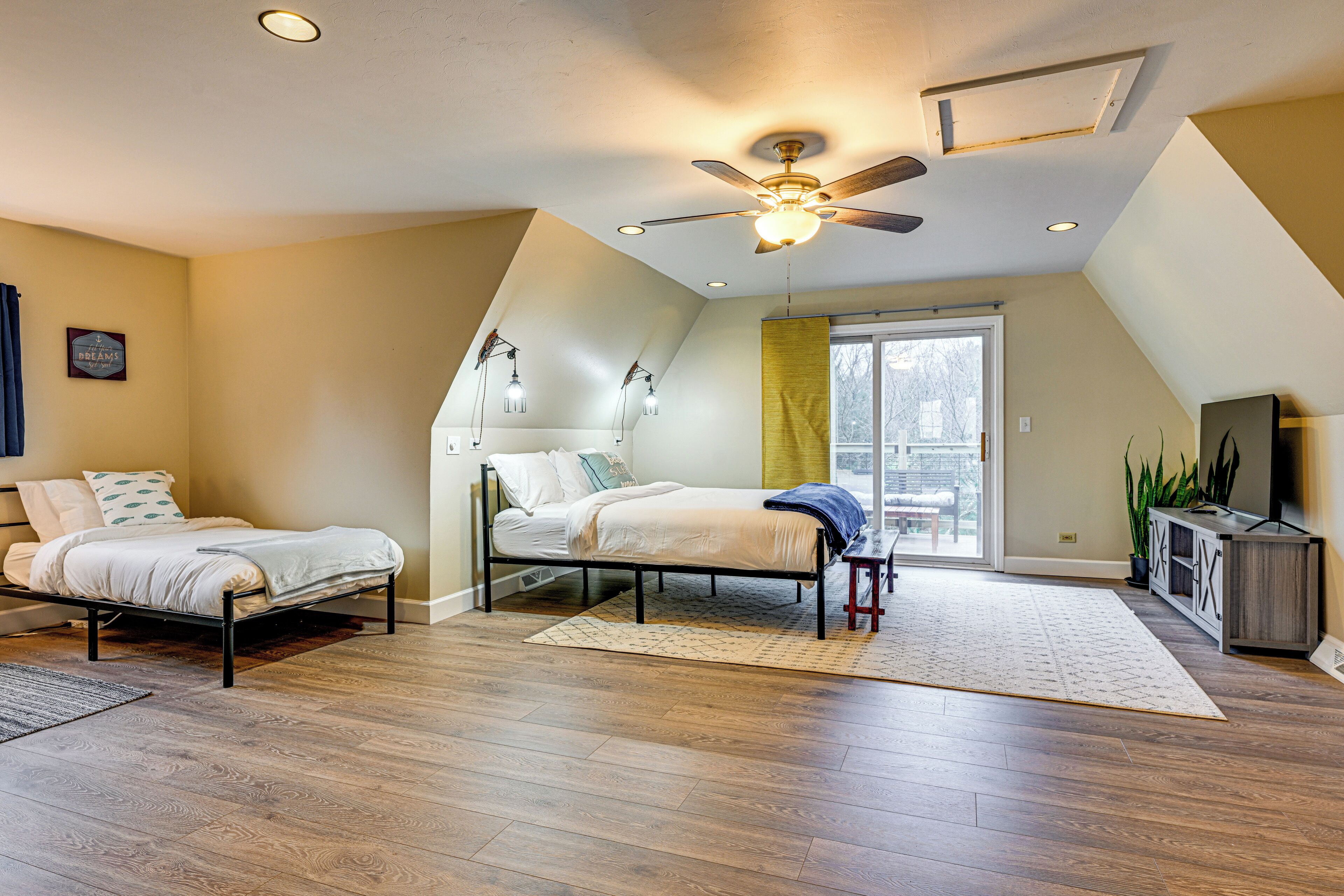 A bedroom with two single beds, a ceiling fan, a large window, and a TV stand.