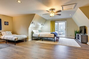 Un dormitorio con dos camas individuales, un ventilador de techo, un ventanal grande y un mueble para televisión.