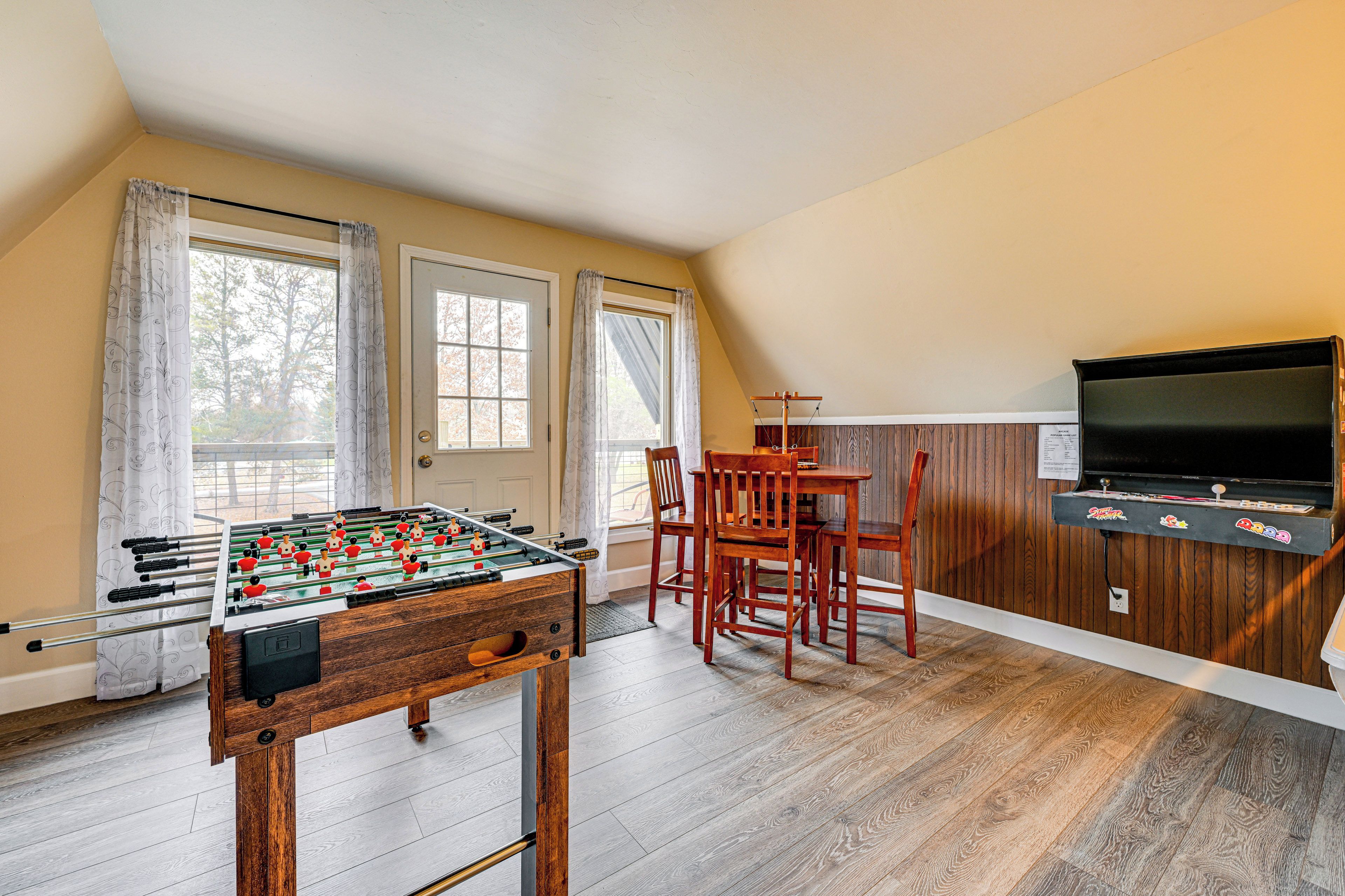 A room with a foosball table, a television, and a dining area with chairs and a table.