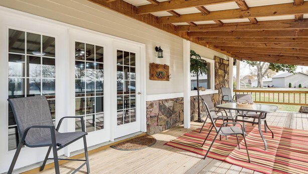 A covered patio with a wooden ceiling, a stone wall, and a dining area with a table and chairs. - Deck & Yard: Wolf Creek Waterfront Home in Grove! (Grove)
