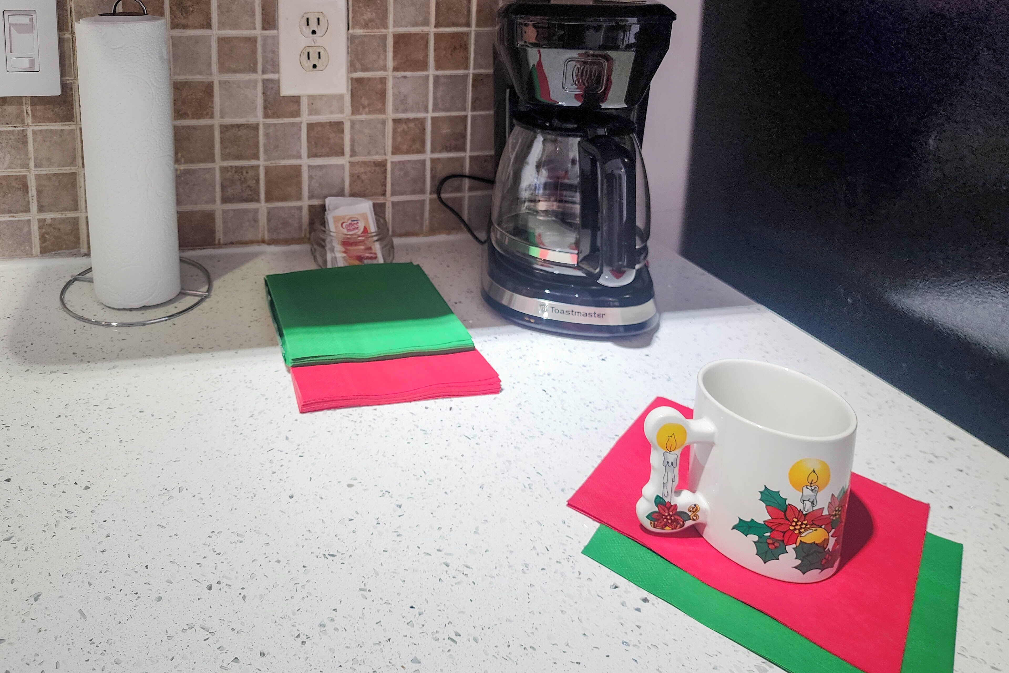 Eine Küchenarbeitsplatte mit Kaffeemaschine, Küchenpapierrolle und einem Stapel farbenfroher Servietten.