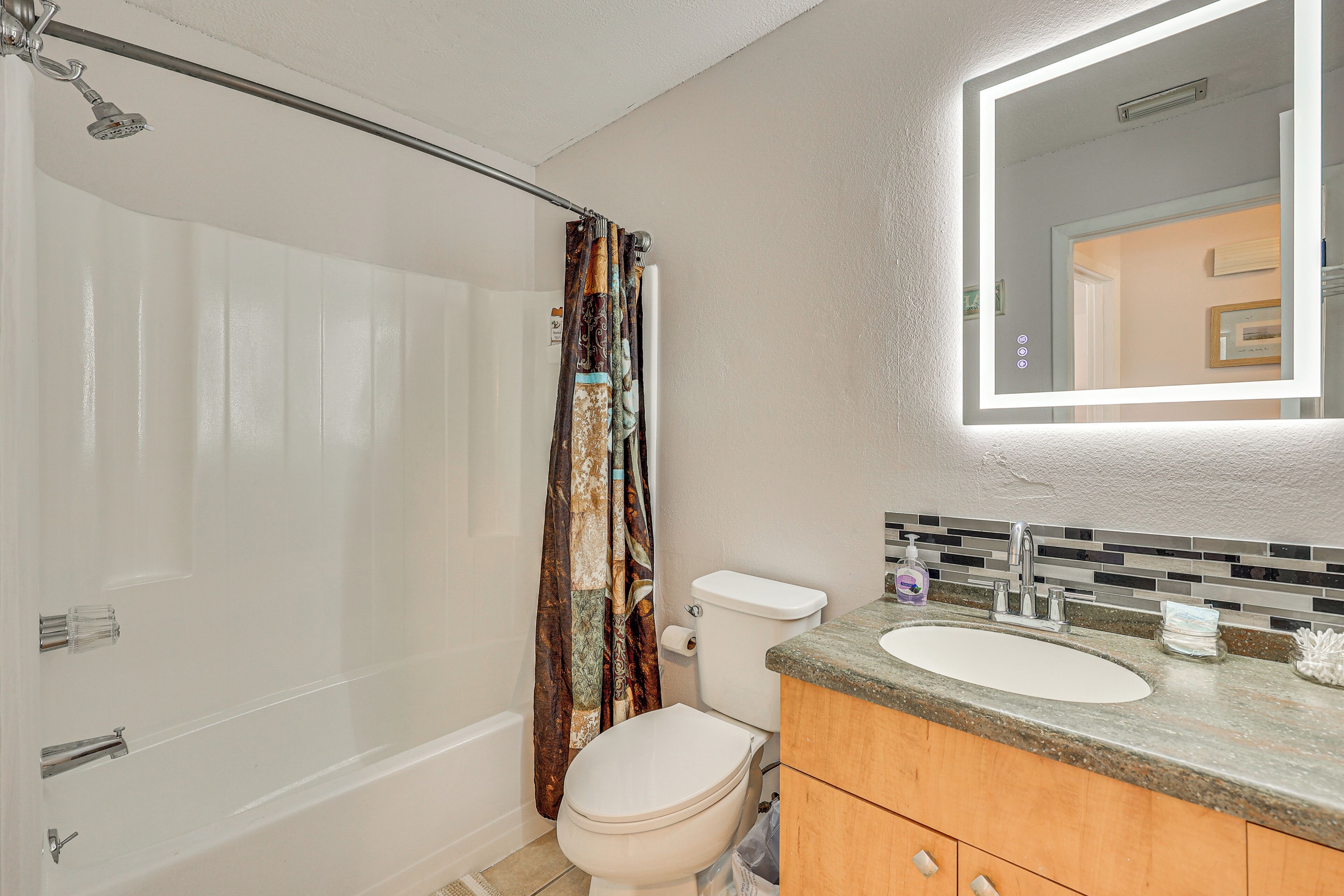 A bathroom with a shower, toilet, sink, and mirror.